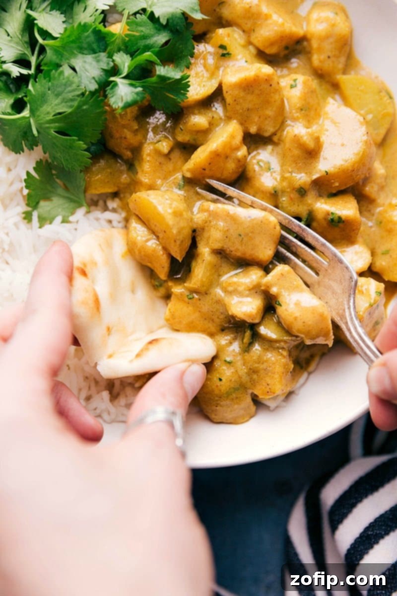 Vibrantly colored Yellow Chicken Curry served over a bed of fluffy white rice, with a side of naan bread ready for dipping. The dish showcases tender chicken pieces and chunks of baby gold potatoes in a rich, creamy sauce, garnished with fresh herbs.