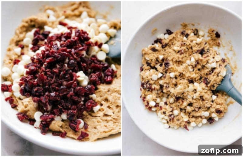 Final Touches to Cranberry Oatmeal Cookies: Expertly Folding in Cranberries and White Chocolate Chips Close-up shot of dried cranberries and white chocolate chips being stirred into cranberry oatmeal cookie dough for a final mix, highlighting the vibrant colors and rich texture.