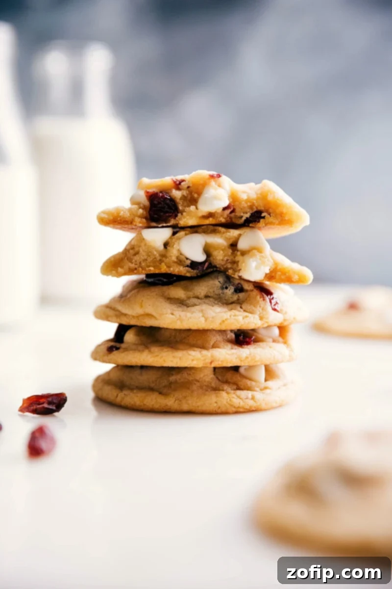 Stack of white chocolate cranberry cookies split open, revealing a gooey, warm interior with melted white chocolate and cranberries. The texture is soft and inviting.