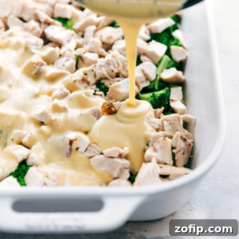 Adding Cheesy Sauce - The Making of a Perfect Casserole A creamy, golden-yellow cheese sauce being generously poured over layers of broccoli and chicken in a casserole dish, preparing it for baking.