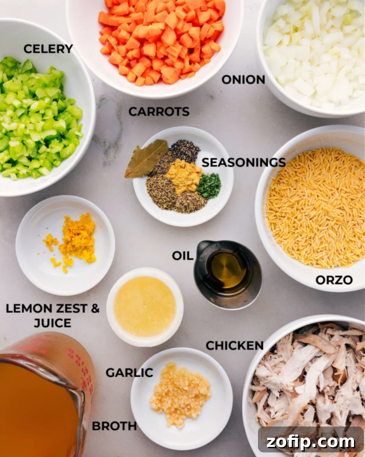 Assorted fresh ingredients for lemon orzo chicken soup displayed beautifully: lemons, shredded chicken, orzo pasta, chopped vegetables (carrots, celery, onion), and fresh herbs.