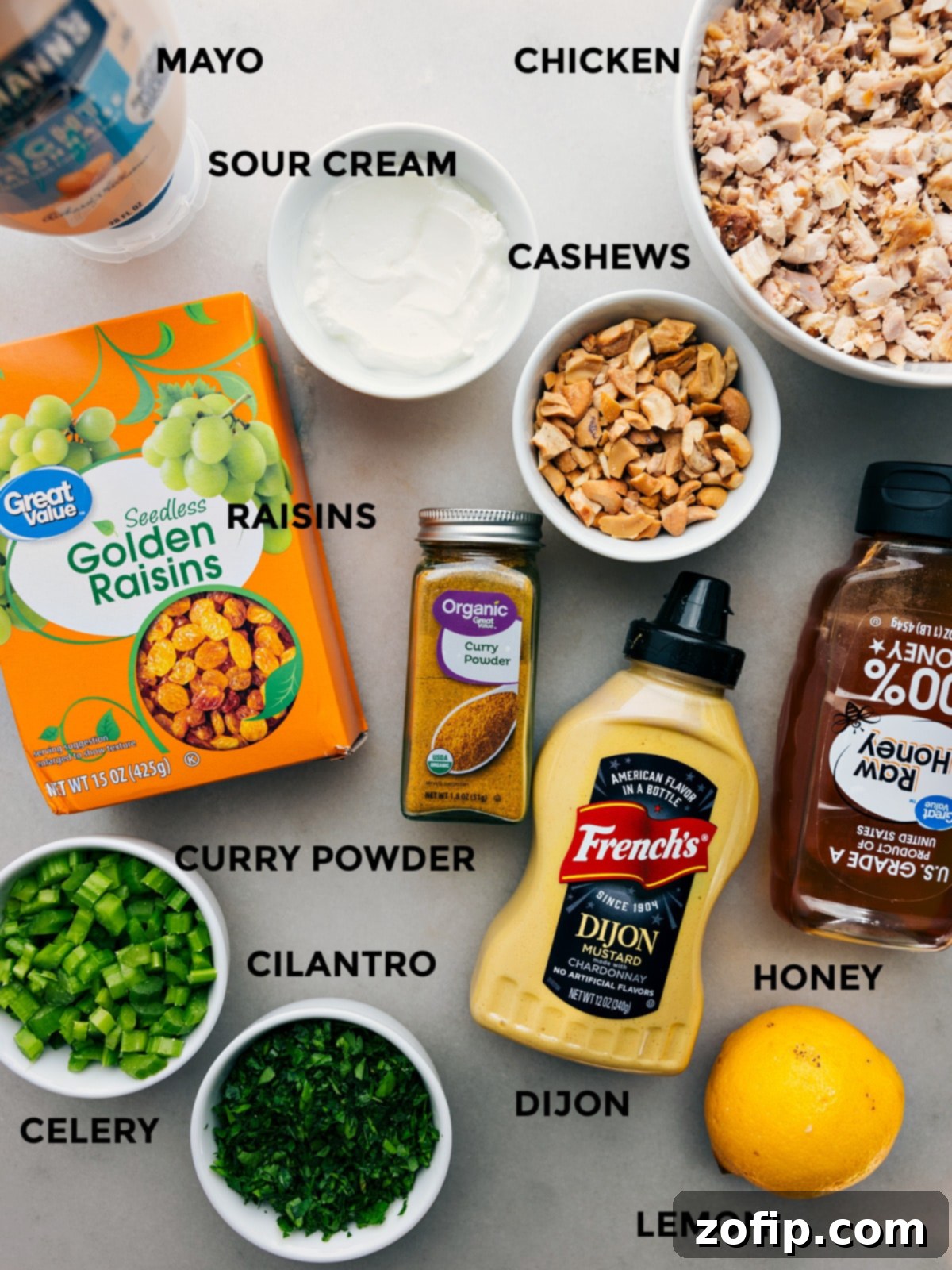 All the ingredients for Curry Chicken Salad prepped and laid out for easy assembly, including mayonnaise, sour cream, shredded chicken, cashews, raisins, cilantro, celery, Dijon mustard, honey, and lemon.