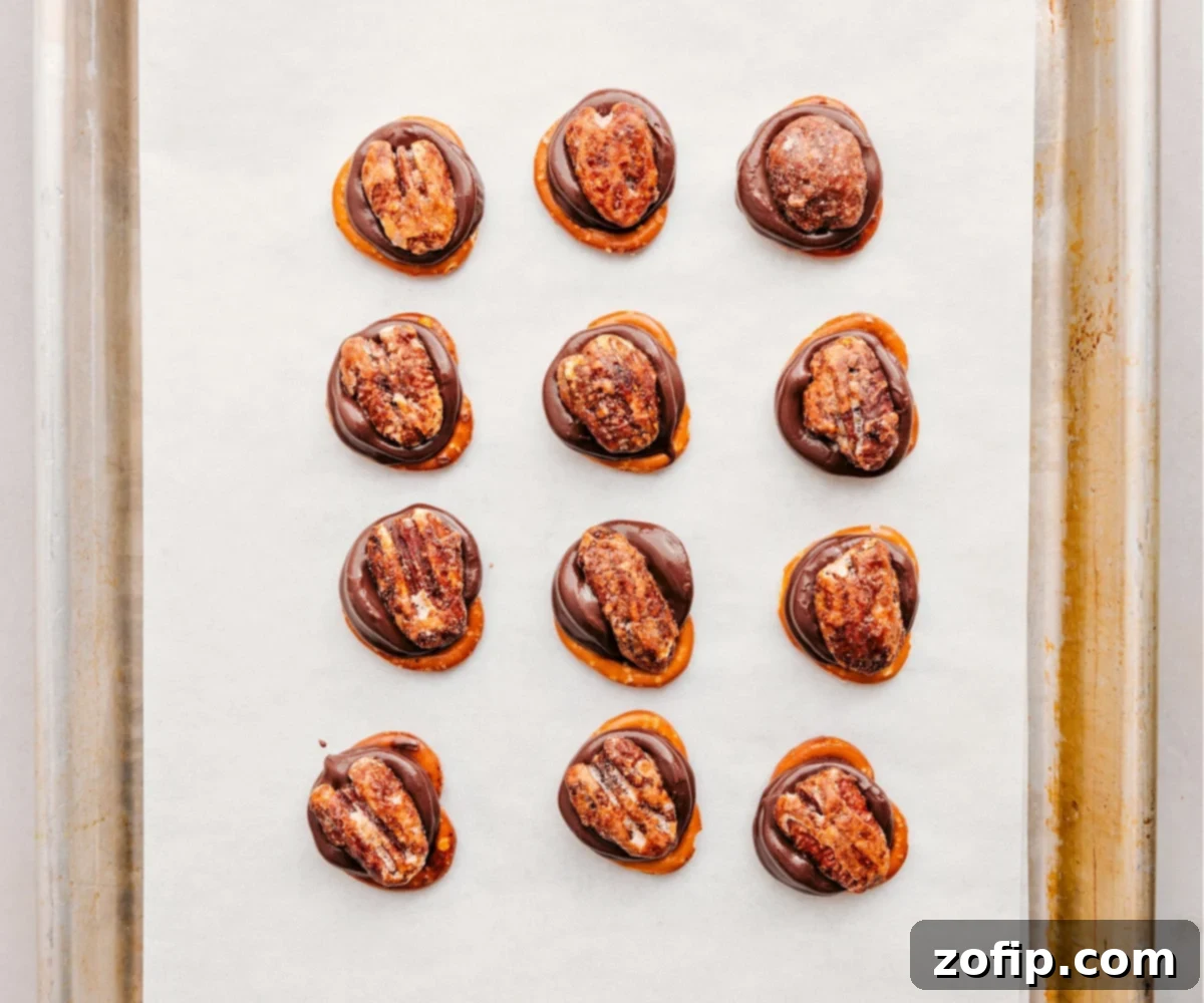 Rolo Pretzel Turtles fresh out of the oven, showing the softened Rolos on pretzels, with pecan halves being pressed onto each one by hand.