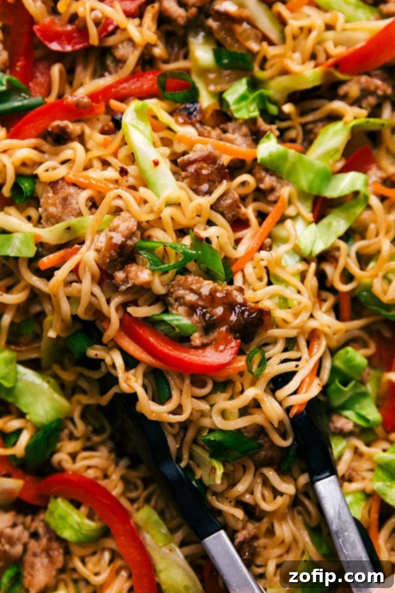 A savory and colorful egg roll noodle dish in a bowl, topped with fresh green onions, ready to be enjoyed. The noodles are coated in sauce, with visible pieces of pork and vegetables.