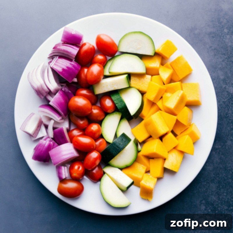 Bright, vibrant, fresh fruit and vegetables including perfectly diced mango, sliced red onion, whole cherry tomatoes, and zucchini on a plate, prepped and ready to be grilled and skewered.