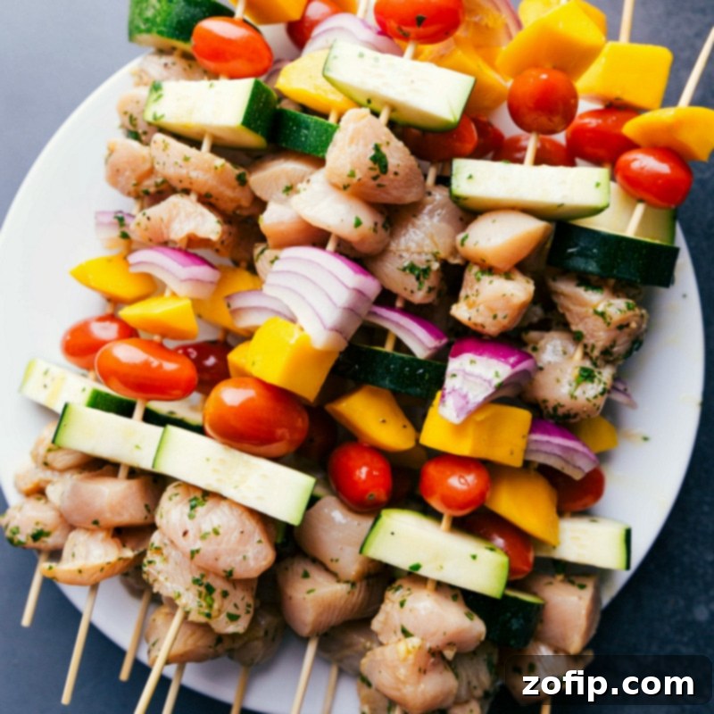 Uncooked chicken kabobs recipe, assembled with marinated chicken, mango, red onions, and cherry tomatoes, prepared and ready for grilling.