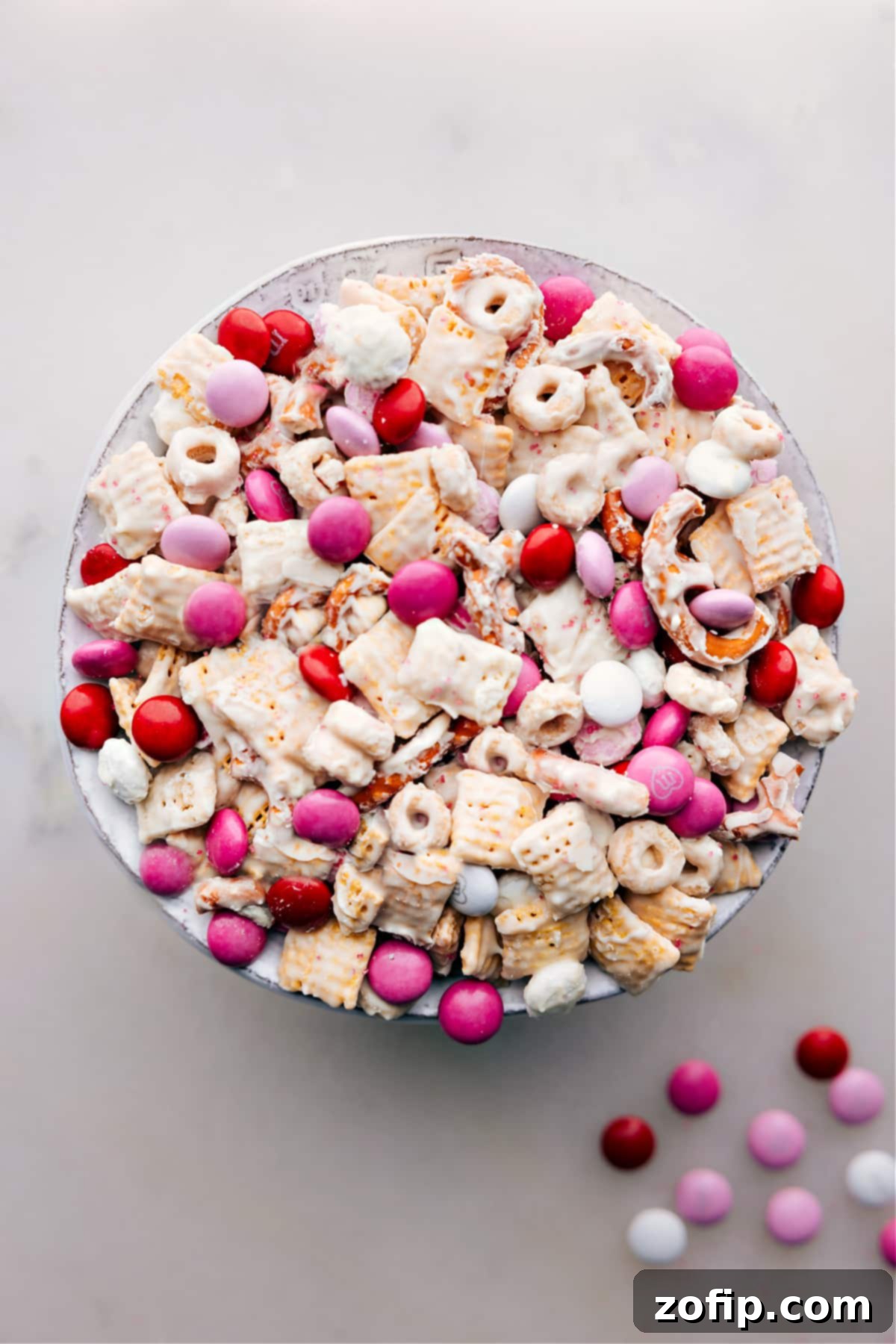 A vibrant bowl of Valentine Snack Mix, featuring red, pink, and white M&M's, pretzels, and cereal coated in white chocolate, ready to be enjoyed.