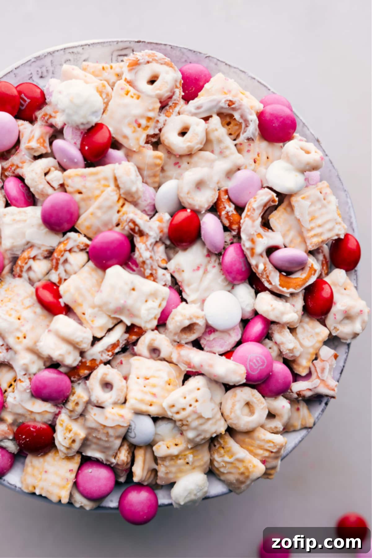 A large bowl filled with a delightful Valentine Snack Mix, showcasing a variety of textures and colors from cereals, pretzels, and M&M's coated in white chocolate.