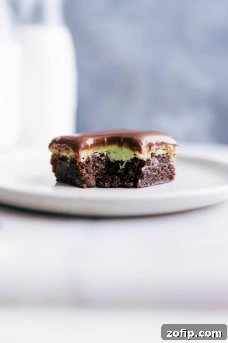 A delicious chocolate mint brownie square on a white plate with a bite taken out of it, revealing its fudgy interior and vibrant mint frosting layer.