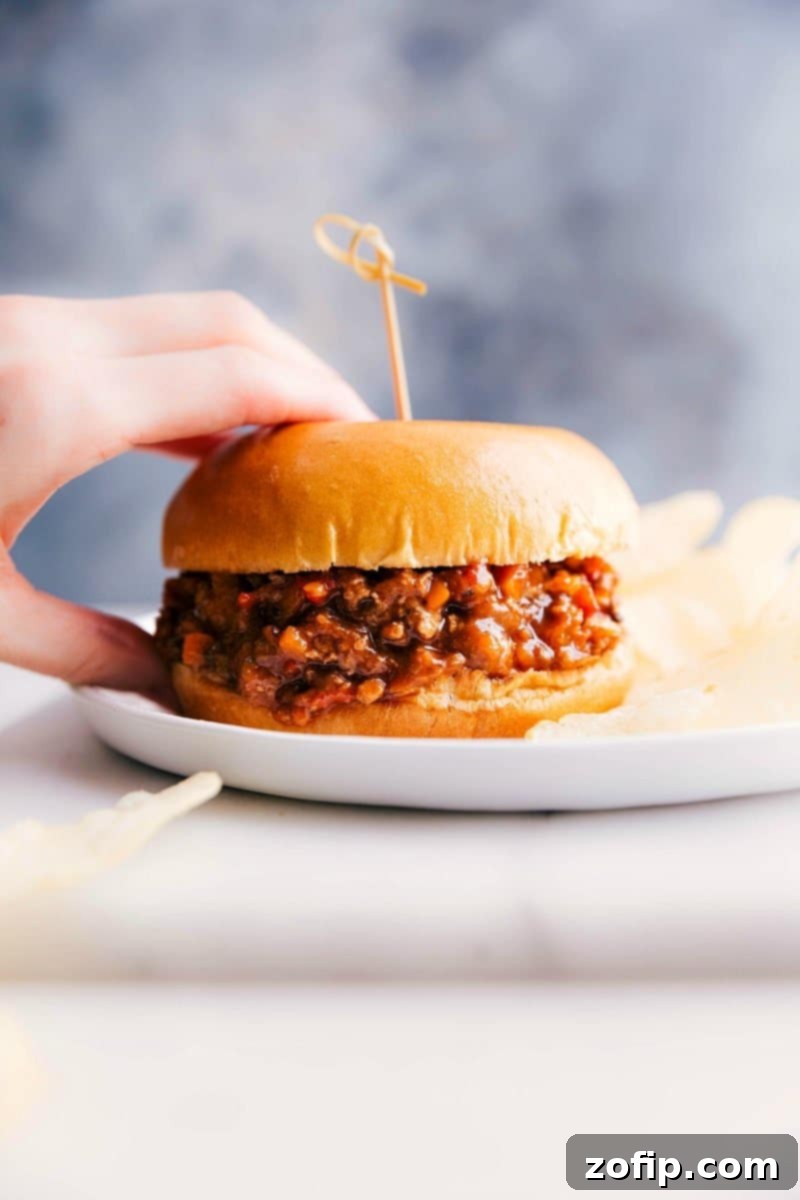 A delicious turkey sloppy joe sandwich, held in a hand, showcasing the messy, saucy filling, ready to be enjoyed.