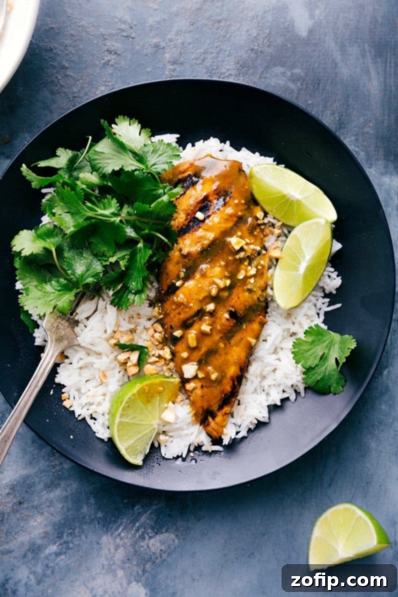 Savory grilled curry chicken, showcasing its golden-brown exterior and charred marks, resting atop a bed of fluffy coconut rice, garnished with fresh cilantro and lime wedges, ready to be served for a delightful meal.