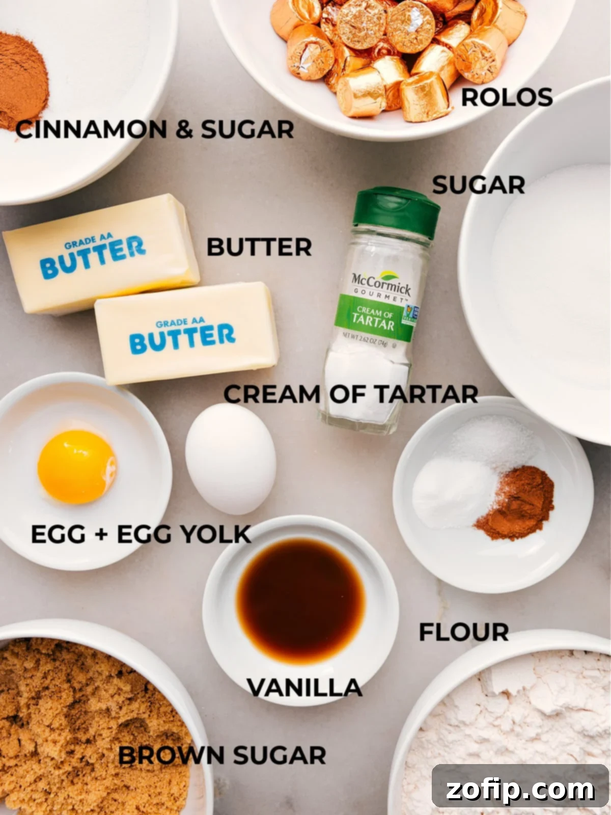 An assortment of essential baking ingredients for making caramel snickerdoodles, featuring butter, cinnamon, sugar, flour, eggs, and vanilla extract.