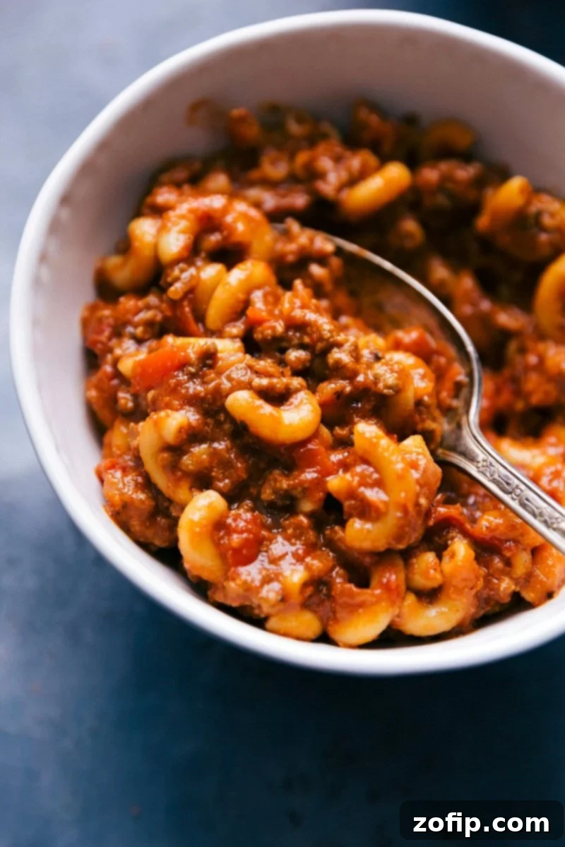 A steaming bowl of homemade American Goulash with a spoon, garnished with fresh parsley and ready to be enjoyed.
