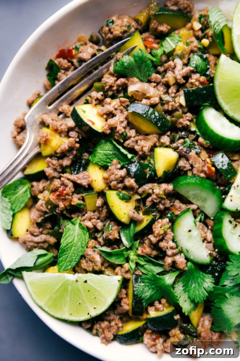Ready-to-Eat Beef Larb with Fresh Lime and Herb Garnish A beautifully plated Beef Larb meal, garnished with vibrant green herbs and a fresh lime wedge, with a fork resting beside it, ready to be enjoyed.