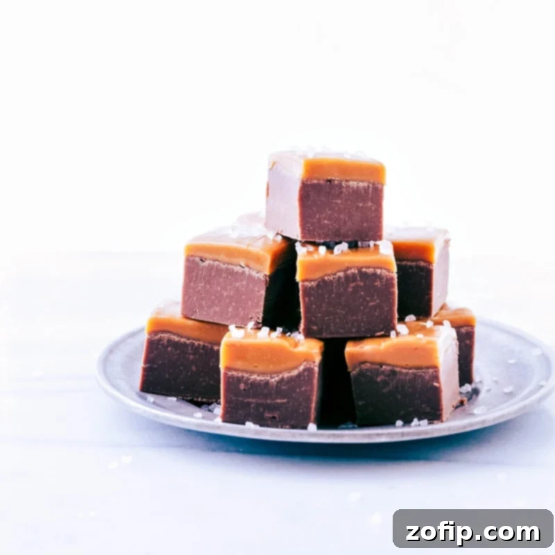 Various cubes of homemade Microwave Fudge, neatly stacked on a white plate, ready to be enjoyed as a sweet treat or gifted.