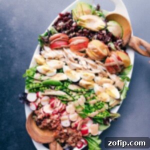 A generous serving platter heaped with a cobb salad masterpiece, boasting meats, fresh vegetables, fruit, and drizzled with creamy balsamic dressing.