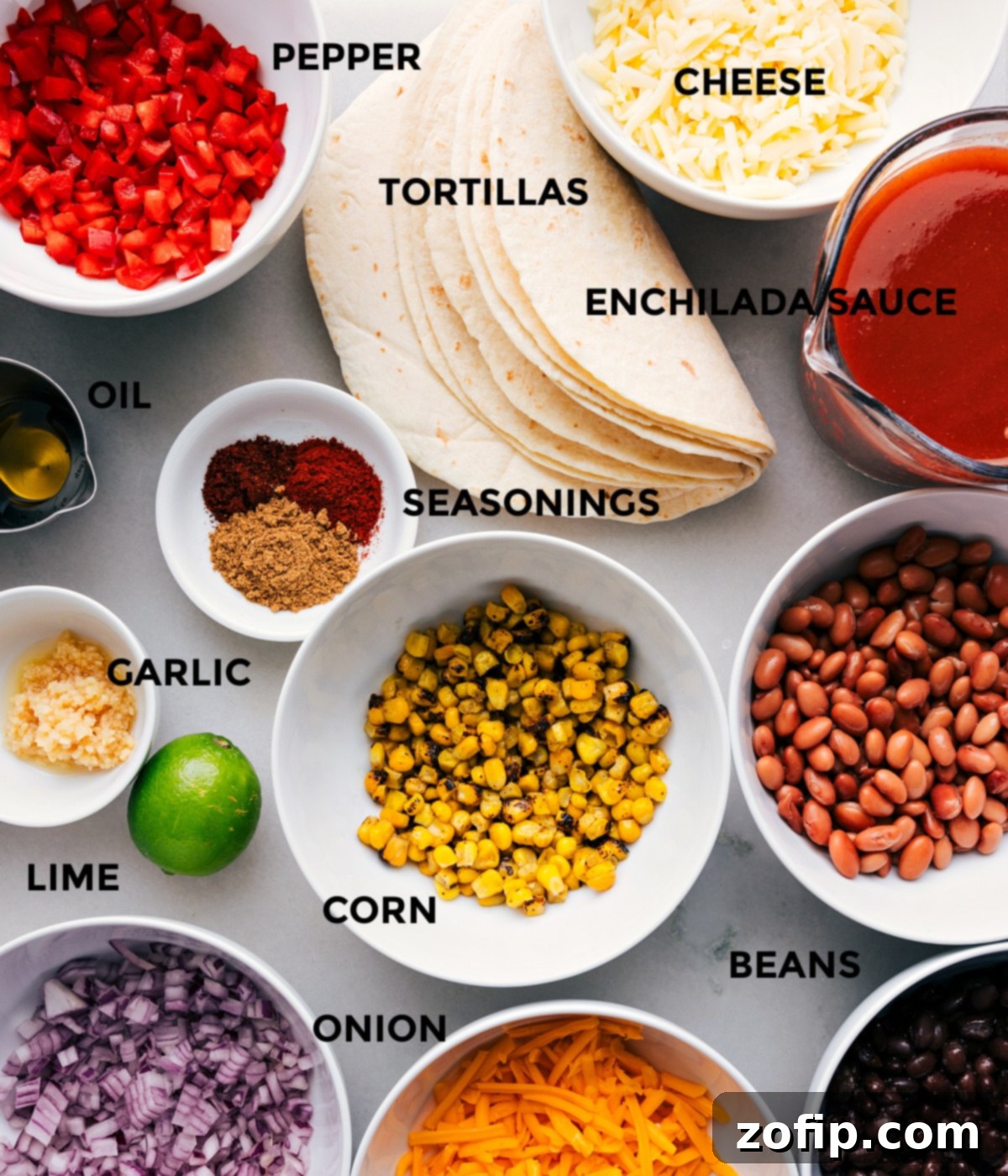 A colorful array of ingredients prepped and ready for making vegetarian enchiladas, including diced red onion and bell pepper, cans of beans, frozen corn, tortillas, enchilada sauce, and shredded cheese.