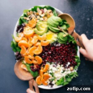 Citrus Ruby Salad 2 Fresh ingredients for the orange pomegranate salad in a bowl including orange slices, pomegranate seeds, mixed greens, walnuts, and feta cheese, ready for mixing.