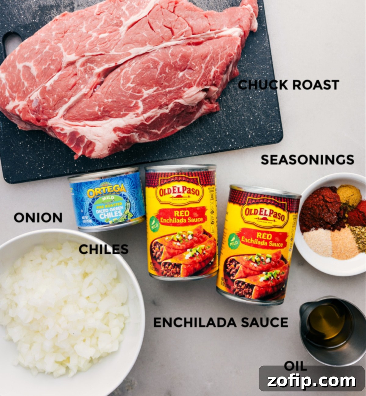 All the essential ingredients for making delicious shredded beef tacos, prepped and ready for assembly, including a beef chuck roast, enchilada sauce, various seasonings, diced onion, mild green chiles, and olive oil.