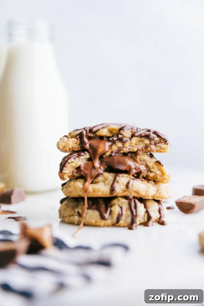 Gooey Caramel Oatmeal Cookies with Chocolate Drizzle Stack of freshly baked Caramel Oatmeal Cookies with a chocolate drizzle, one broken in half to reveal the molten Rolo caramel and chocolate center.