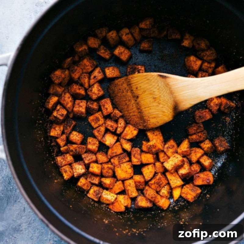 Sautéing Sweet Potatoes with Seasonings - Preparing for Sweet Potato Quinoa Chili Sweet potatoes being expertly sautéed in a pan with a blend of seasonings, infusing them with a rich, aromatic flavor before they join the rest of the ingredients for the sweet potato quinoa chili.