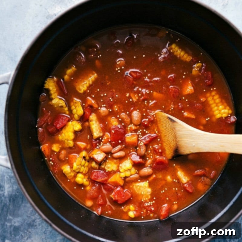Combining Veggies and Beans in Pot - Creating a Flavorful and Complementary Mix for Quinoa Chili A colorful array of vegetables and beans are carefully poured into the pot, joining the cooked sweet potatoes and quinoa. The vibrant mix is then gently stirred, blending delicious and complementary flavors together for the quinoa chili.