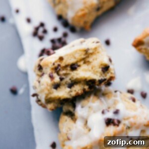 Homemade Chocolate Chip Scones 4 A stack of warm chocolate chip scones with one having a bite taken, showing a flaky interior.