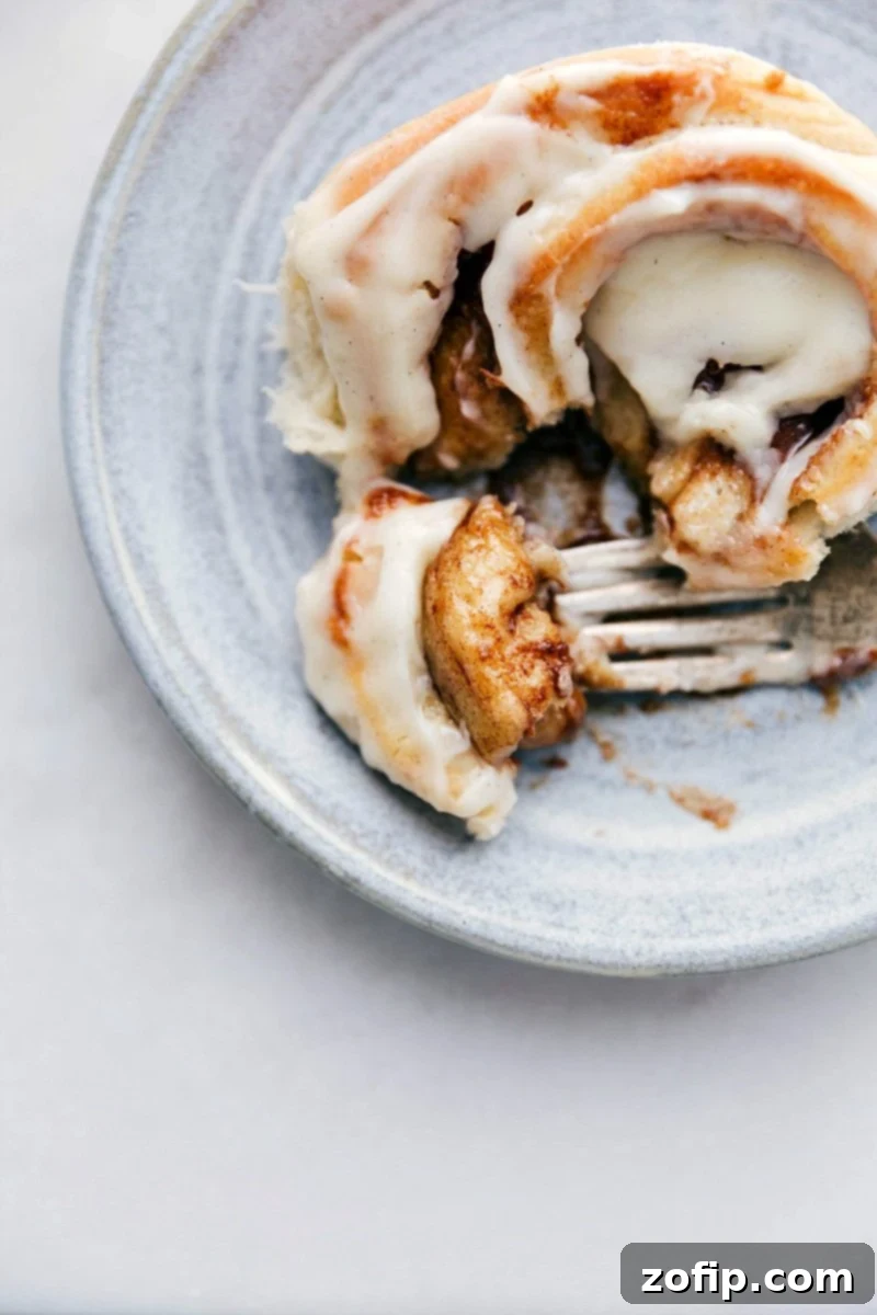 Gooey Homemade Cinnamon Roll with Frosting Up-close photo of a Homemade Cinnamon Roll with a bite taken out of it, showing its gooey center.