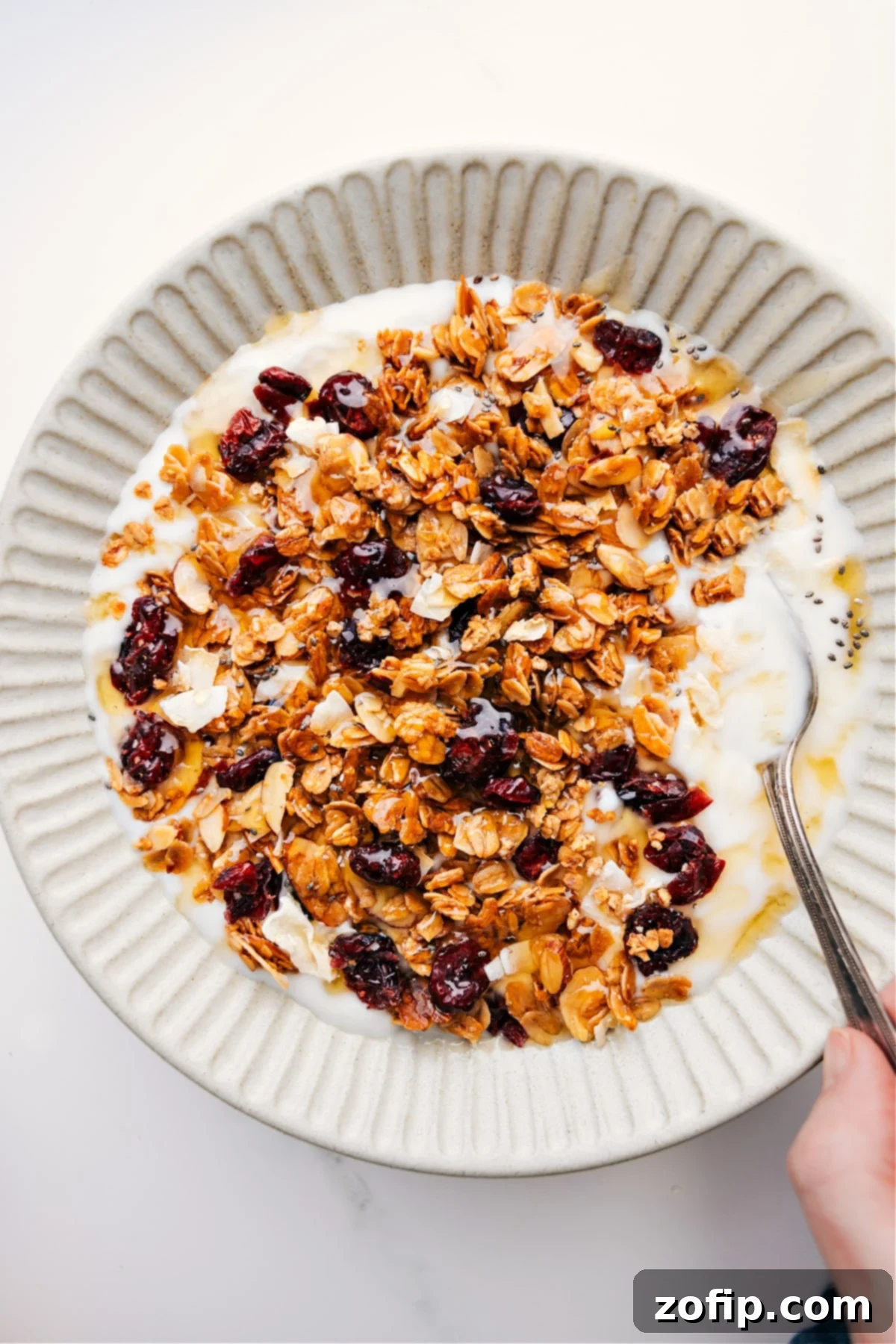 Golden-brown Honey Almond Granola generously sprinkled over creamy Greek yogurt, adorned with fresh blueberries and a delicate drizzle of extra honey, promising a delightful breakfast or snack experience.