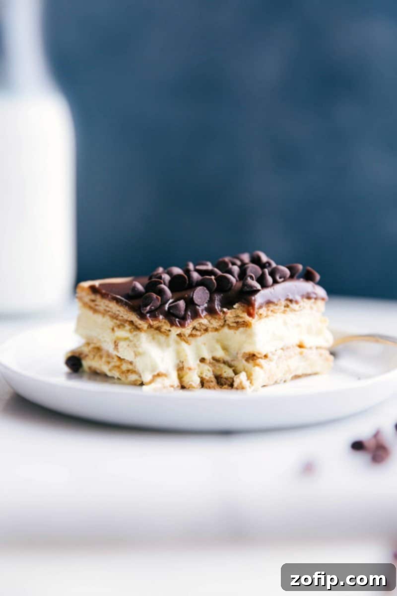 Perfect Slice of No-Bake Eclair Cake with Creamy Center A delicious slice of Eclair Cake with a bite taken out, revealing its creamy layers of graham cracker, vanilla pudding, and rich chocolate ganache. The cake sits on a white plate, ready to be enjoyed.
