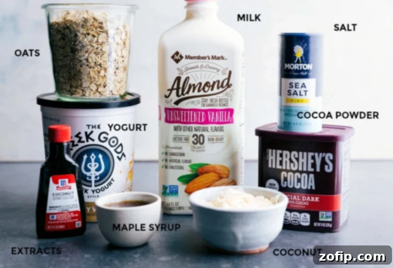 All the core ingredients required for crafting the perfect batch of Almond Joy Overnight Oats, meticulously displayed: a carton of unsweetened vanilla almond milk, a bowl of creamy Greek yogurt, old-fashioned rolled oats, a container of rich cocoa powder, and other essential items.