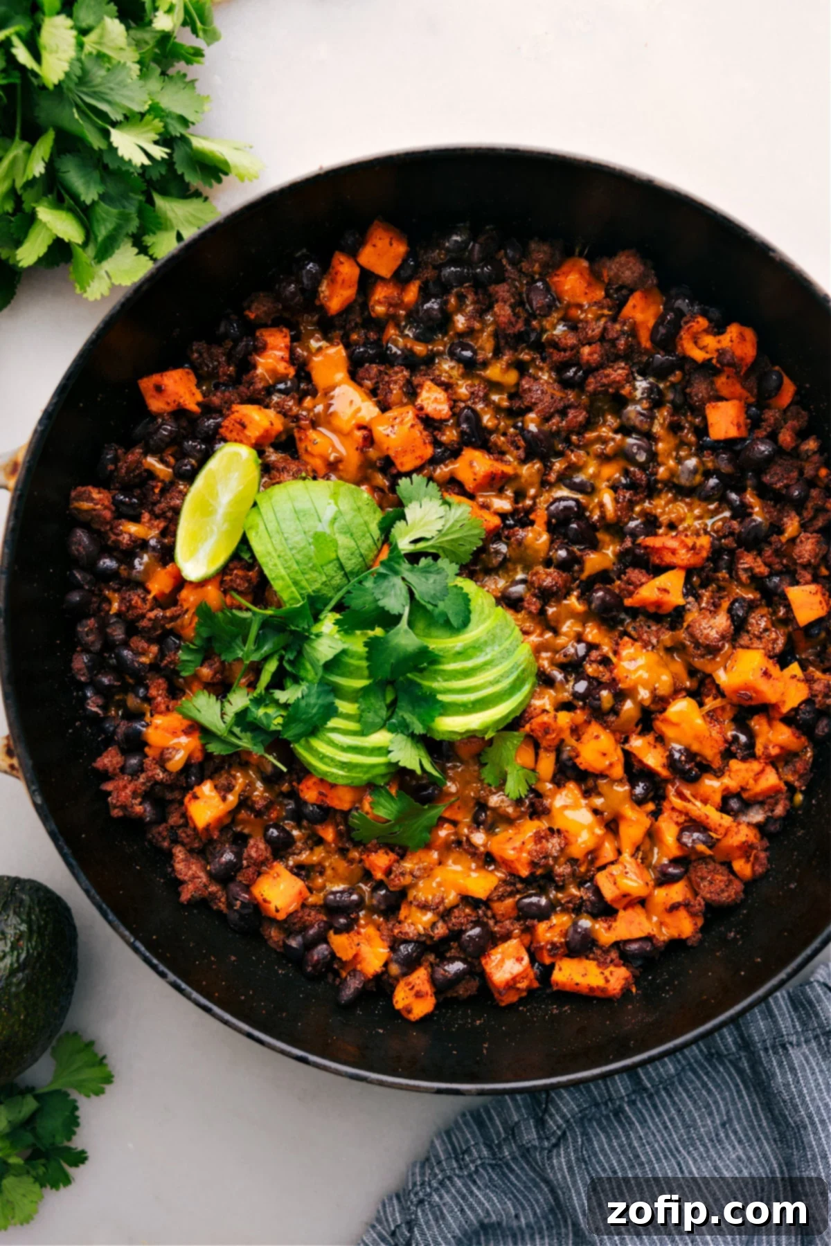 Ground Turkey Sweet Potato Skillet straight from the stove, topped with melty cheese, fresh avocado, and cilantro, highlighting its vibrant and appetizing appearance.