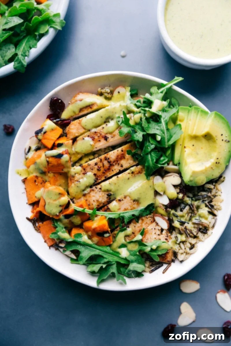 A beautifully arranged chicken and wild rice bowl, featuring grilled chicken slices, fluffy wild rice, cubed sweet potatoes, and a generous drizzle of creamy green sauce, highlighting a healthy and delicious meal.