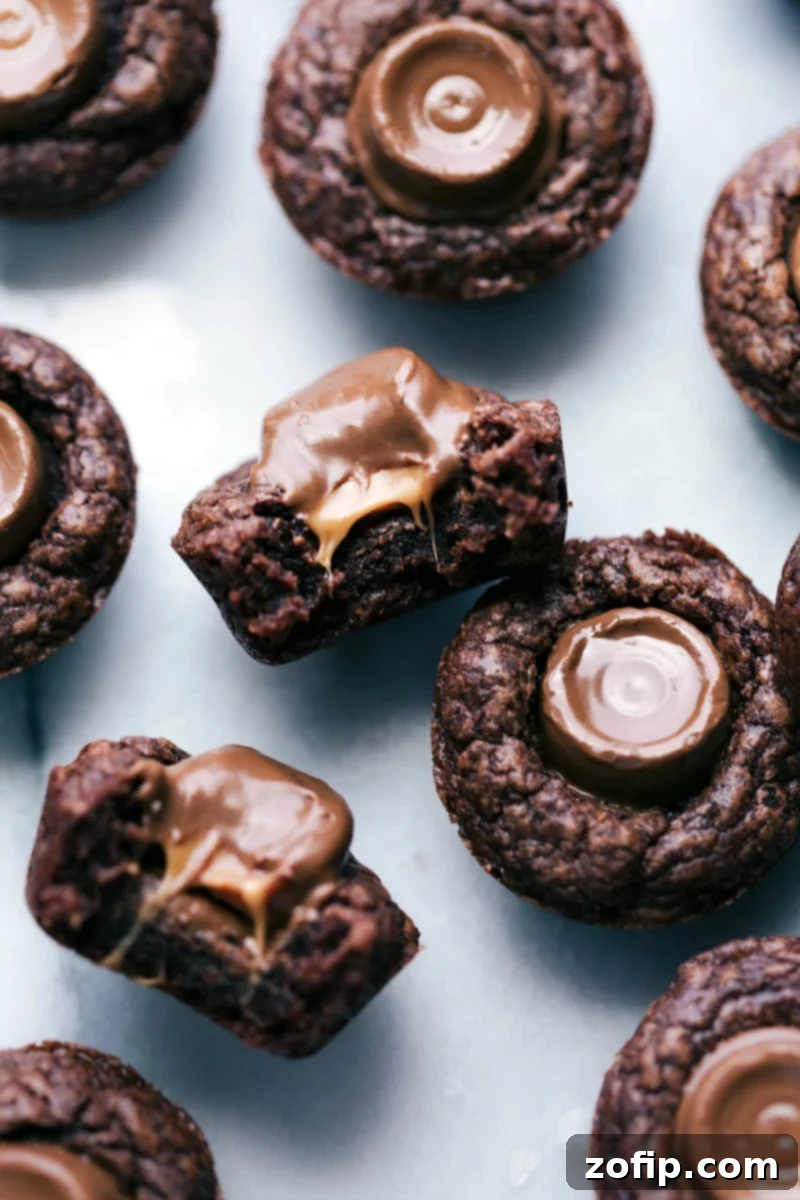 A close-up of mini brownie bites with Rolos, one cut in half revealing its warm, gooey caramel core, against a blurred background of more brownies.