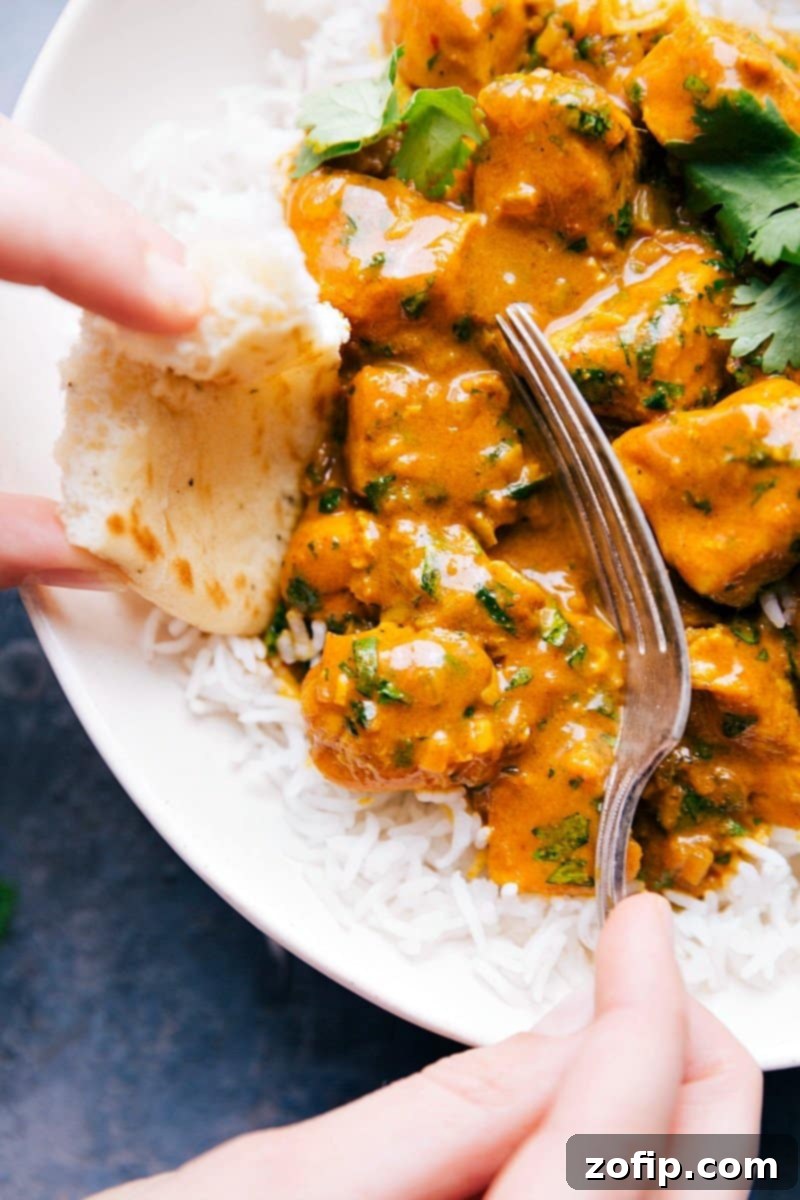 Up-close image of Curry Chicken being scooped up with a fork and naan bread. Highlights the rich texture of the sauce and tender chicken.