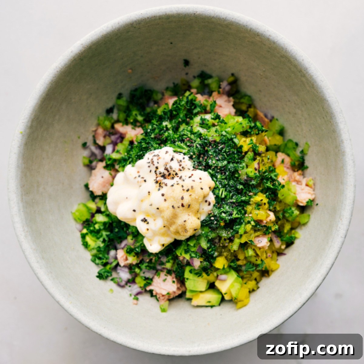 The creamy elements of the avocado tuna salad dressing, including mashed avocado, mayonnaise, Dijon mustard, and seasonings, are being combined in a bowl, ready to be whisked into a smooth mixture.