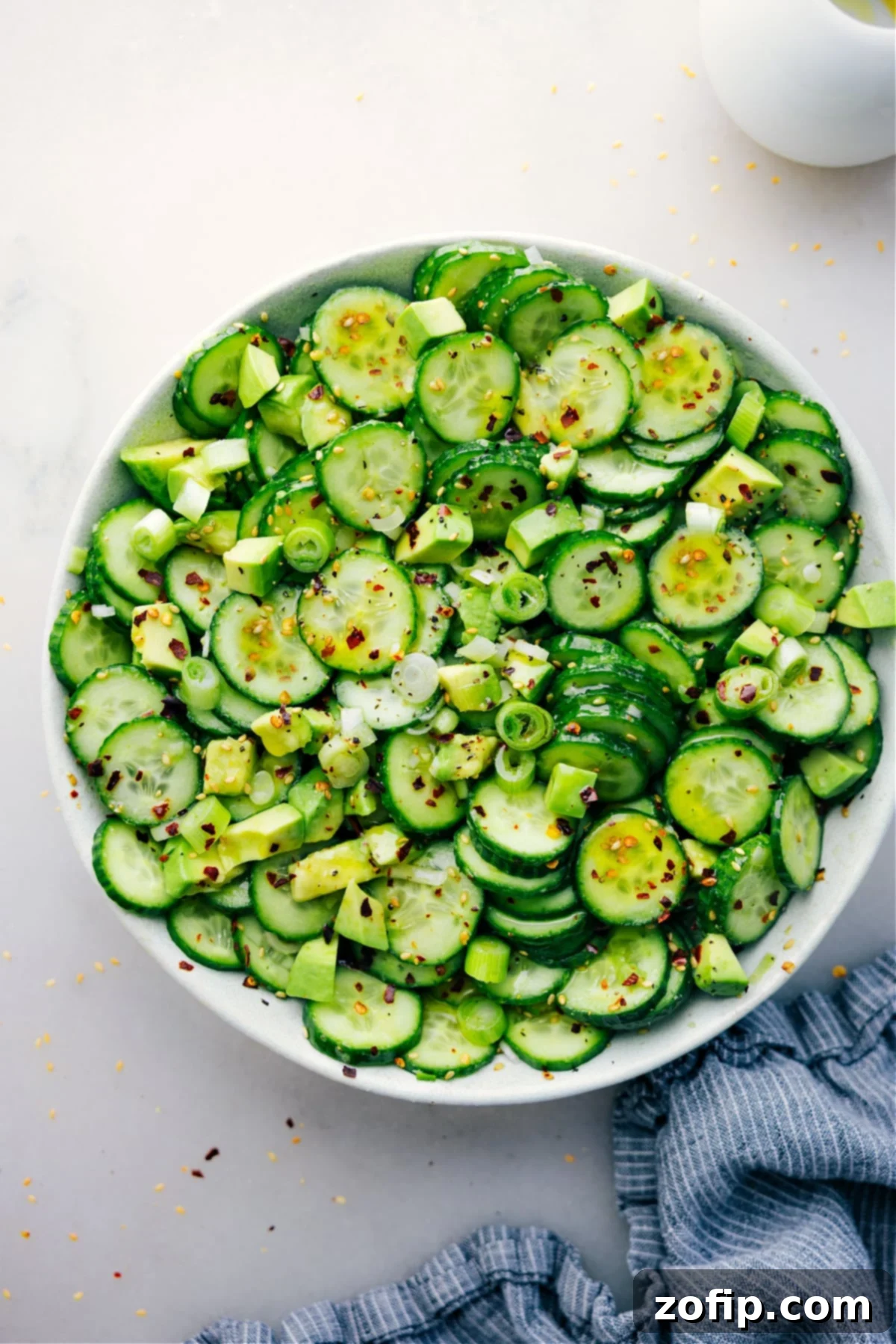 A beautifully presented bowl of Asian Cucumber Salad, vibrant with fresh green cucumbers, avocado, and green onions, lightly drizzled with sesame dressing and ready to be enjoyed.