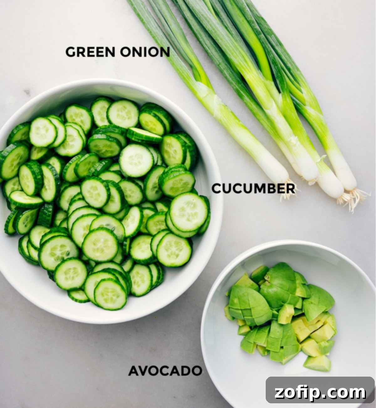 Individual ingredients for the simple Asian Cucumber Salad laid out: thinly sliced cucumbers, precisely chopped avocado, and vibrant sliced green onions, all prepped for easy assembly.