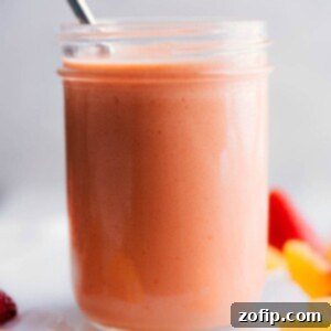 Velvet Peach Refreshment 2 A tall glass of creamy peach smoothie topped with fresh peach slices and a wide straw.