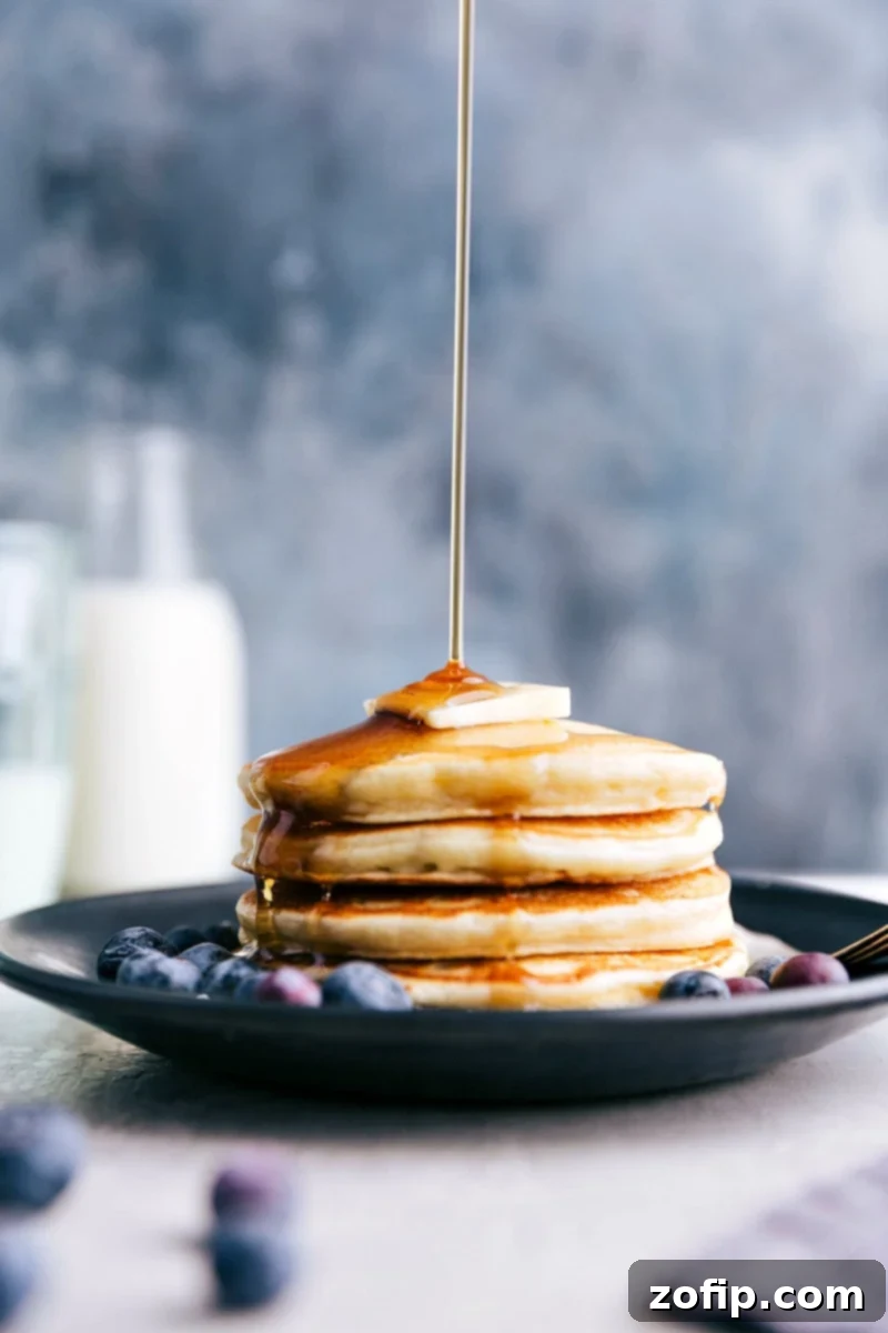 Pack your pancakes with nutrition and protein for a fulfilling breakfast! Golden Greek Yogurt Pancakes being drizzled generously with maple syrup, ready to be enjoyed.