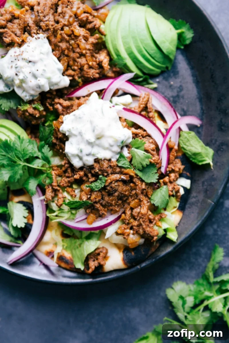 Ground Beef Naan Tacos - Flavorful and Satisfying Quick Meal Idea A vibrant spread of Ground Beef Naan Tacos, showcasing rich ground beef, crisp lettuce, red onion, a drizzle of creamy herb sauce, and fresh cilantro on charred naan bread, perfect for a delicious meal.