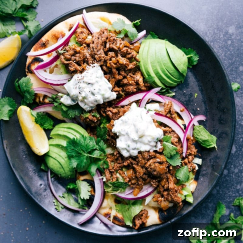 Ground Beef Naan Tacos - A Visually Stunning and Flavorful Feast A perfectly plated Ground Beef Naan Taco, showcasing the rich, spiced ground beef, fresh lettuce, thinly sliced red onion, and a generous drizzle of the creamy raita sauce, garnished with fresh cilantro and a lime wedge. The vibrant colors and textures promise a delightful culinary experience.