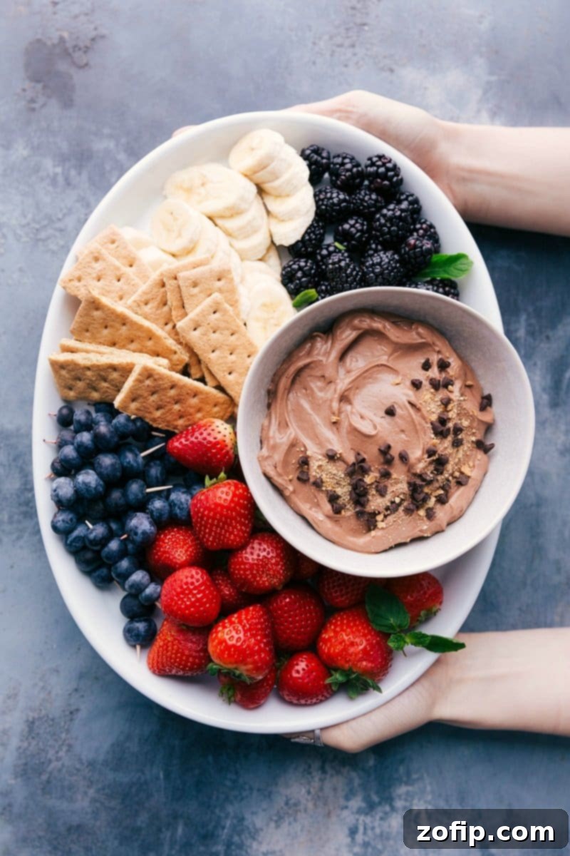 Luscious Chocolate Dip for Fruit artfully arranged with a vibrant assortment of fresh berries, sliced strawberries, bananas, and crisp graham crackers, inviting guests to indulge.