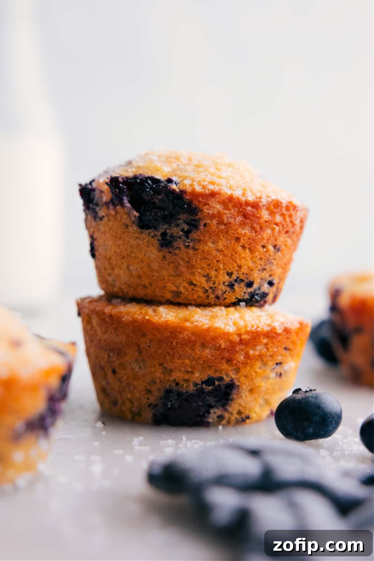 The Best, Delicious & Healthy Blueberry Muffins Ready to Enjoy Several healthy blueberry muffins, golden brown with a sparkling sugar topping and visible blueberries, stacked neatly on top of each other, invitingly displayed.