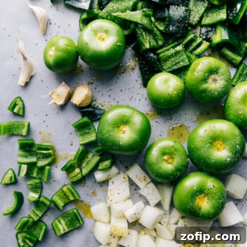 Crafting your own Green Enchilada Sauce means a depth of flavor unmatched by any canned alternative. This recipe uses quality seasonings, vegetable broth, and olive oil to complement the fresh tomatillos, peppers, onions, and garlic. Recipe via ChelseasMessyApron.com #enchiladas #greensauce #greenenchiladas #tomatillos #mexican #spicy #tacotuesday A vibrant selection of fresh ingredients: tomatillos, poblano peppers, jalapeños, onions, and garlic laid out, ready for making green enchilada sauce.