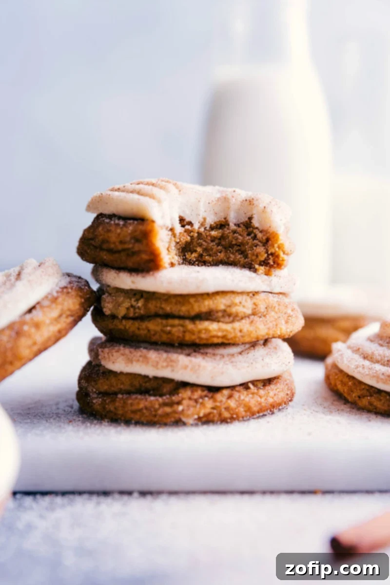 Stacked pumpkin cinnamon roll cookies with a bite taken out of the top one, revealing their fluffy interior and delightful frosting.