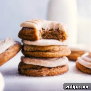 Stacked pumpkin cinnamon roll cookies with a bite taken out of the top one, revealing their fluffy interior and delightful frosting.