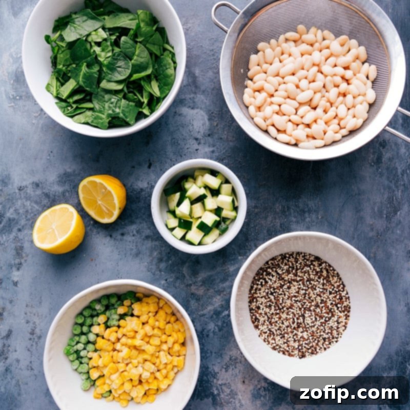 Assorted fresh ingredients for a healthy minestrone soup laid out in individual bowls, including chopped carrots, celery, onion, garlic, white beans, quinoa, herbs, and canned fire-roasted tomatoes, ready for preparation.
