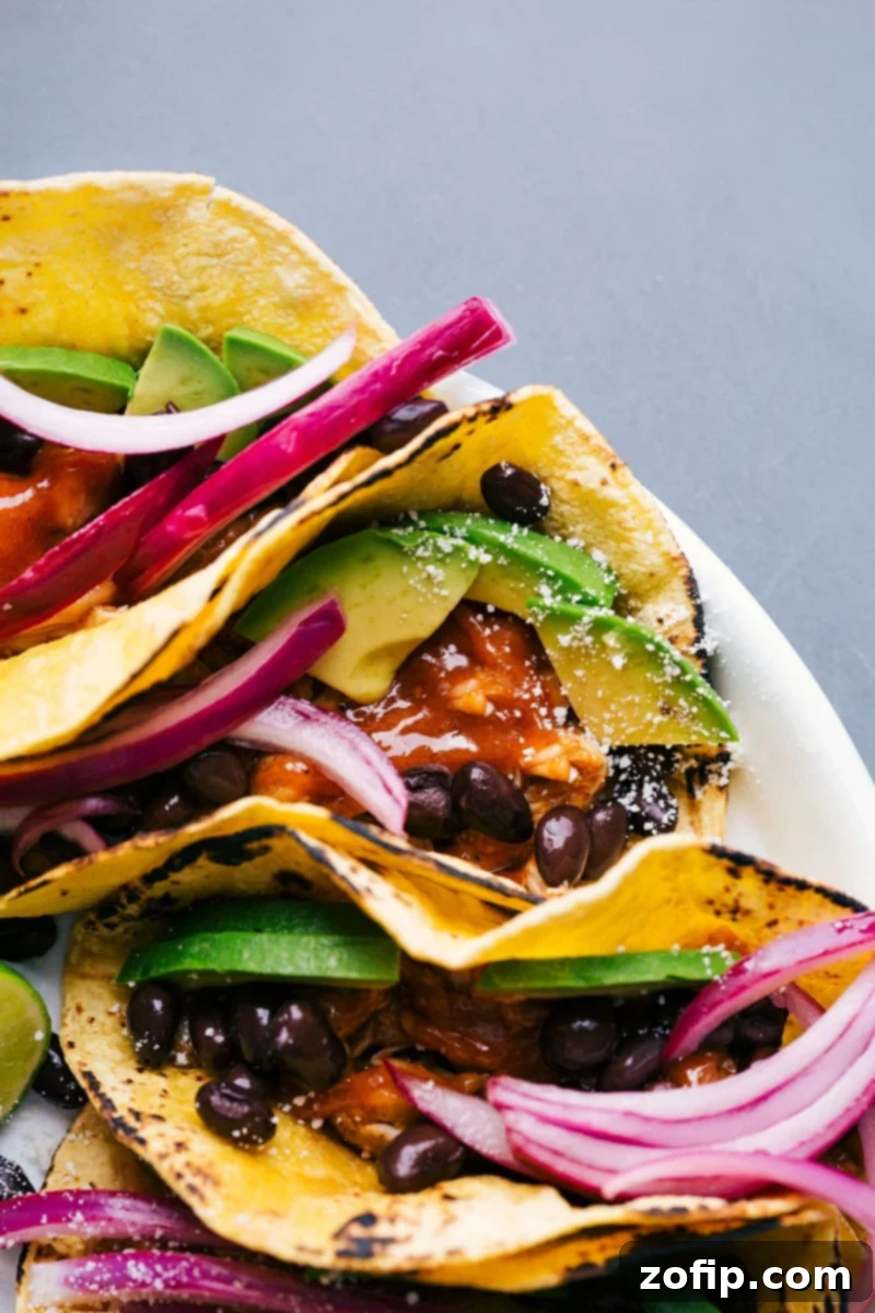 A vibrant platter of Chipotle chicken tacos, generously topped with fresh cilantro, creamy avocado, black beans, and tangy pickled red onions, ready to be served.