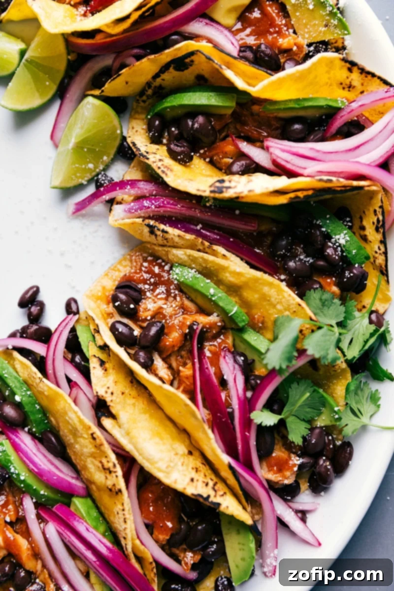 Beautifully assembled chipotle chicken tacos, garnished with fresh cilantro, a sprinkle of Cotija cheese, and vibrant pickled red onions, arranged on a rustic platter.